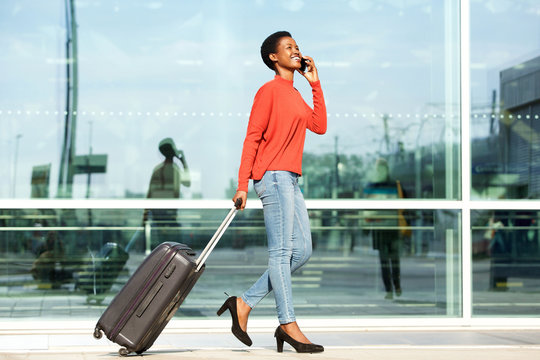 Full body profile of happy female traveler walking .with suitcase bag and cellphone