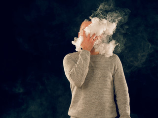 smoking man in e-cigarette smoke on black background