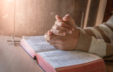 Close up hands of young man praying with bible on wooden table. christian concept.