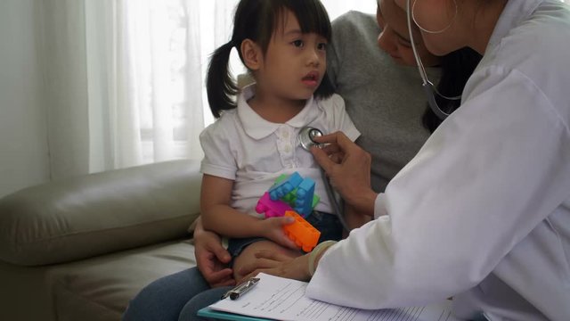 Medium shot of female doctor examining with stethoscope little Asian girl sitting on mothers knees