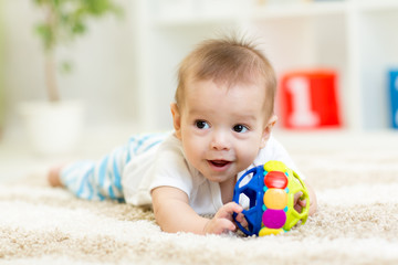 Fototapeta na wymiar Adorable baby having fun with toy on cozy rug. Happy cheerful kid boy playing on the floor