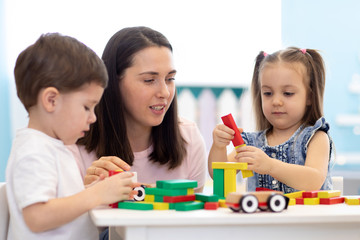 Mother or teacher with children building block toys at home or daycare. Kids playing with color blocks. Educational toys for nursery and kindergarten.