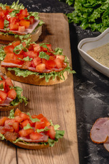 Italian homemade bruschetta with chopped tomatoes, salad leaves, ham and sauce on grilled crusty bread. horizontal view