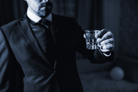 Close up of stressful businessman in suit standing in hotel room and drinking alcohol. Alcohol addiction concept.