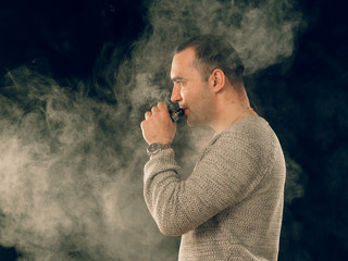smoking man in e-cigarette smoke on black background