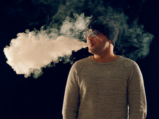 smoking man in e-cigarette smoke on black background