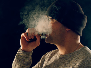 smoking man in e-cigarette smoke on black background