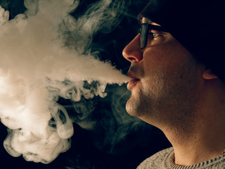smoking man in e-cigarette smoke on black background