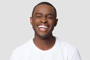 Tuinposter Cheerful happy african millennial man laughing looking at camera isolated on studio blank background, funny young black guy with healthy teeth beaming orthodontic white wide smile head shot portrait © fizkes