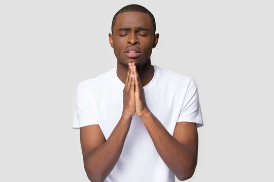 Worried young african american man put hands together ask for help forgiveness in prayer isolated on white studio background, religious christian black guy praying with hope, worship belief concept