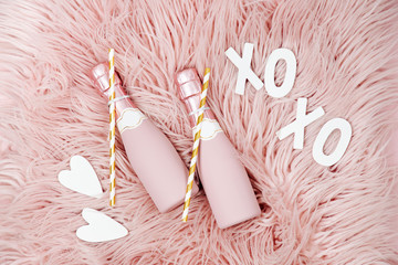 Champagne bottles on pink fluffy fur background. Flat lay, top view