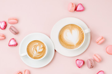 Coffee cups with candys and macaroons on pale pink background. Flat lay, top view