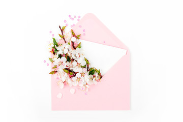 Pink envelope with empty card and a spring flower arrangement. Flat lay, top view.
