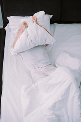 Fototapeta na wymiar depressed woman covering face with pillow while lying in bed at home