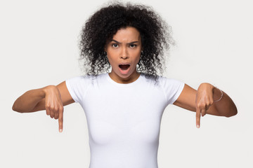 Shocked black woman looking at camera point fingers below indicate unbelievable sale offer,...