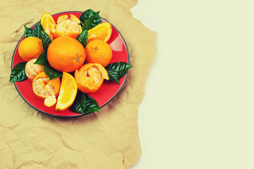 Red plate of oranges and tangerines with green leaves on a light background Top view copy space