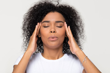 Fototapeta Nervous african woman breathing calming down relieving headache or managing stress, black girl feeling stressed self-soothing massaging temples exhaling isolated on white grey studio blank background obraz