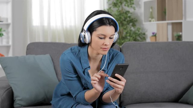 Surprised woman listening to music from cell phone sitting on a couch at home