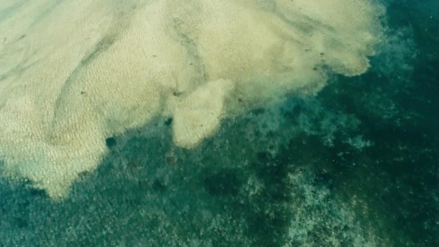 stunning aerial drone footage of a great coral reef meeting a sandy beach in calm weather flat water and incredible colorful sea ocean bed around a small remote isolated tropical island