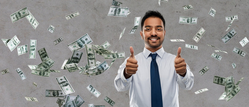 business, office worker and people concept - smiling indian businessman showing thumbs up over money rain on grey background