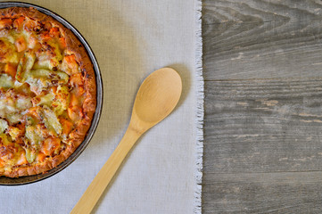 Pie with vegetables and cheese in a vintage pan with a wooden spoon on a white linen napkin on wooden rustic background