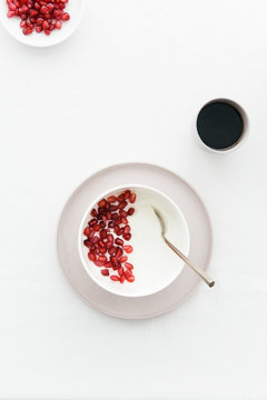 Breakfast table with Greek yoghurt, pomegranate seeds, black coffee, plate and bowl.