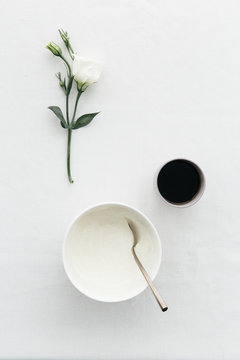 Breakfast table with Greek yoghurt, black coffee and white flower.