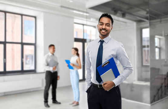 business, realty and people concept - smiling indian businessman or realtor with clipboard over empty office room background