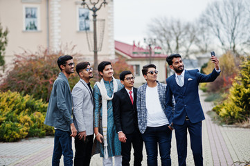 Group of six south asian indian mans in traditional, casual and business wear standing and making selfie at mobile phone together.