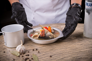 Cook in black gloves is serving fish soup