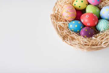 easter, holidays, tradition and object concept - close up of colored eggs in wicker basket on white background