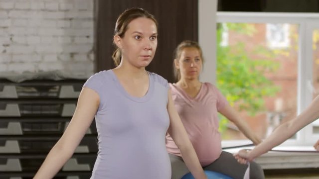 Medium shot of four active pregnant women sitting on stability balls and performing shoulder circles with band during fitness workout