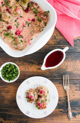 Swedish meatballs in a red cowberry sauce with green onion. White casserole and plate on wooden rustic table, top view
