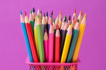 a lot of color pencils in a pink glass on a bright trendy purple background