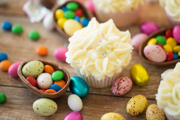 Fototapeta na wymiar easter, food and sweets concept - frosted cupcakes with chocolate eggs and candies on table
