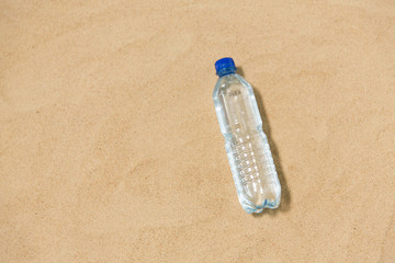 hydration and summer concept - bottle of water on beach sand