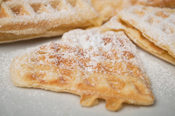 closeup of waffle in shaped heart with sugar in a white plate