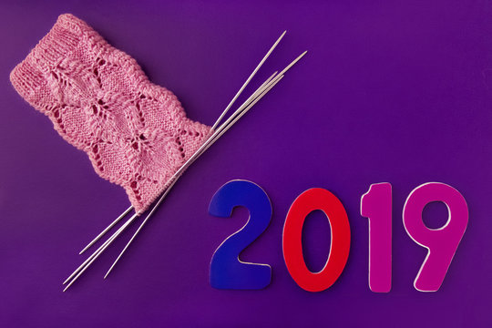 numbers wood 2019 and pink socks made of wool, knitted with an openwork pattern on four knitting needles on purple background