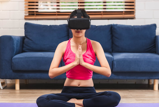 Asian woman use virtural reality glasses headset to training yoga pose online in living room floor at home.self learning,