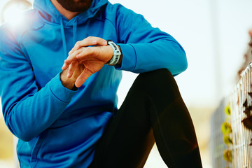 Close up of sporty bearded man kneeling and setting stopwatch. Healthy lifestyle concept.