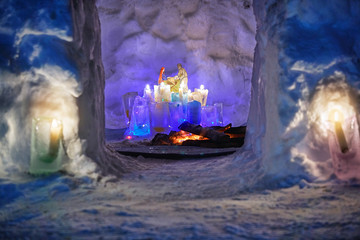 Burth of a Jesus installation inside of snow igloo house with colorful icy plafonds and burning...