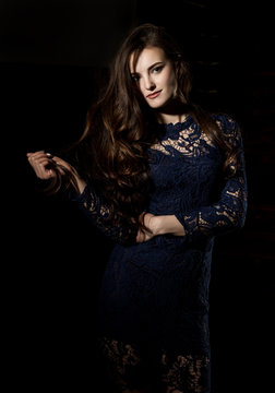 Sensual attractive young woman in a lace dress poses on a dark background