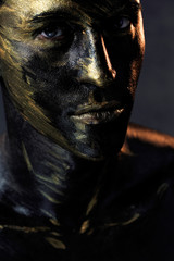 a man in black make-up with gold. portrait of a guy in dark paint with gold. Artistic portrait photography