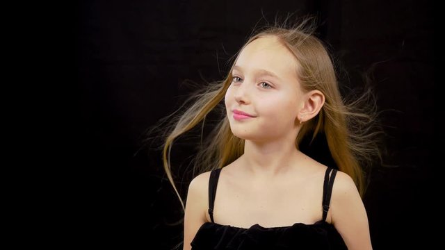 Young caucasian girl portrait at dark background. Long blonde hair smile face. Girl swying tilts head from side to side. Beauty teenage close up person