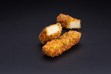 Breaded mozzarella cheese sticks laid out on a black background.