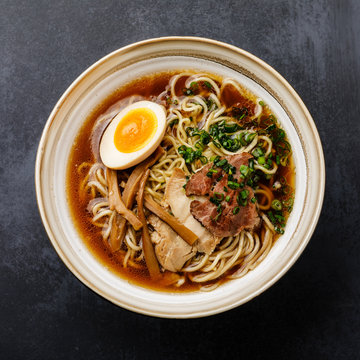 Ramen asian noodle in broth with meat and Ajitama pickled egg in bowl on dark background