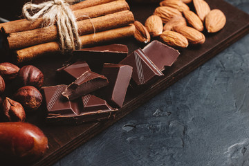 Chocolate cubes, nuts, dates and cinnamon sticks, healthy eating on a dark background
