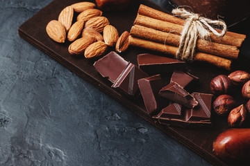 Chocolate cubes, nuts, dates and cinnamon sticks, healthy eating on a dark background