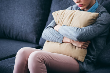 cropped view of woman sitting on couch and holding pillow at home