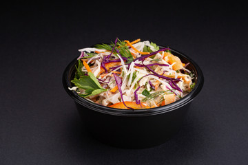 mix vegetables salad with purple cabbage, white cabbage, lettuce, carrot in dark clay bowl on black background.
